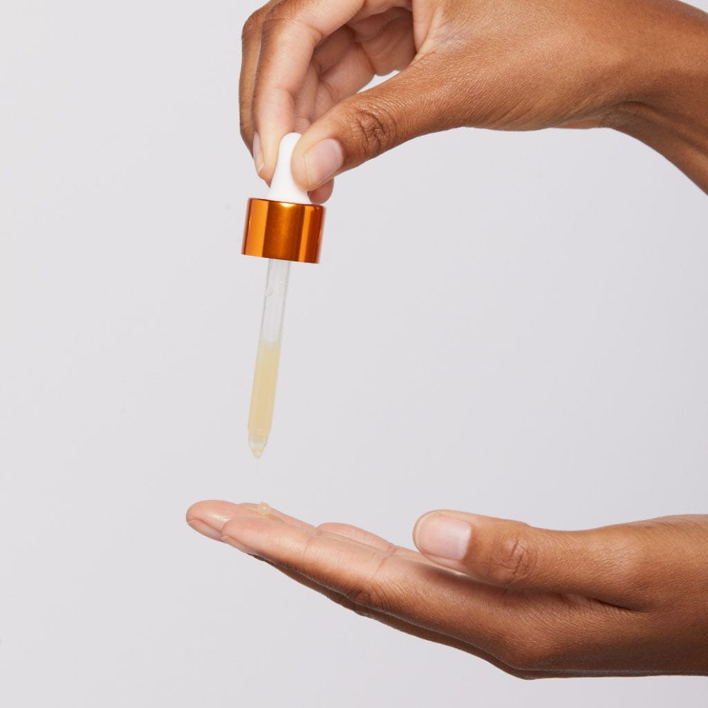 Hand mit Pipette träufelt klare Flüssigkeit auf die andere Hand