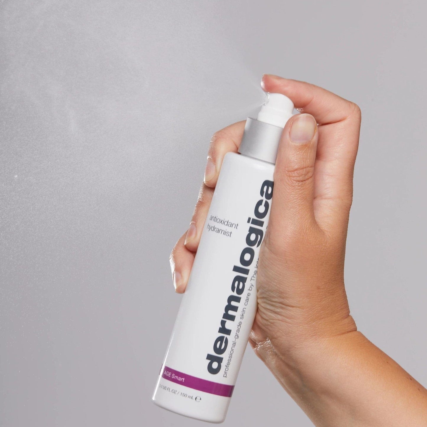 Eine Hand hält eine Flasche Antioxidant Hydramist gegen einen grauen Hintergrund